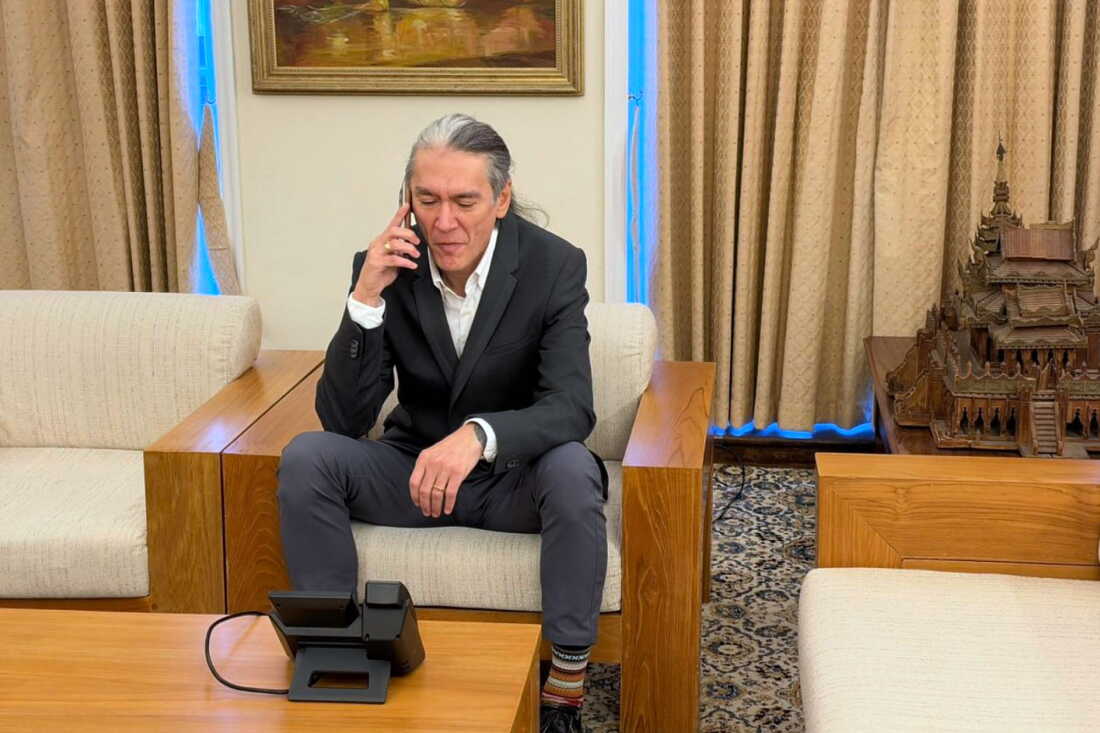 In this photo released by Myanmar's government on Thursday, Kim Aris, son of Myanmar's ousted leader Aung San Suu Kyi, talks on phone with his mother, at the Myanmar Embassy in London.