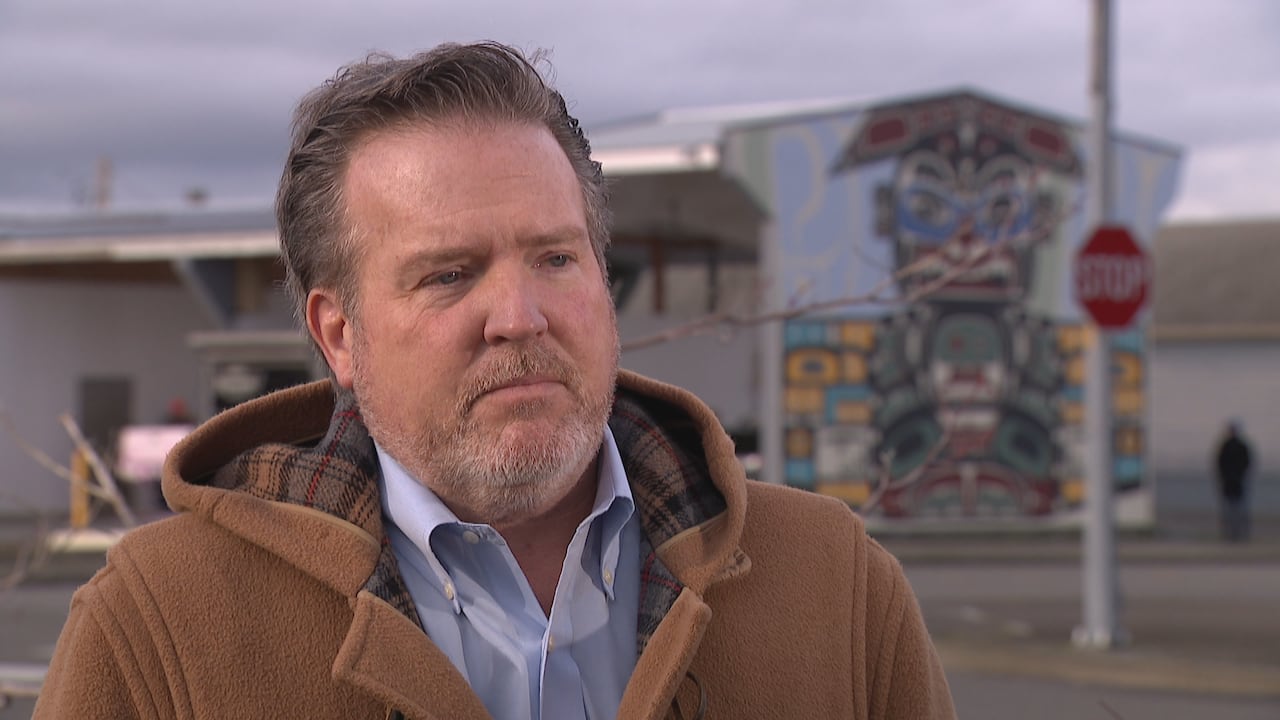 A white man wearing a brown coat is seen outdoors.