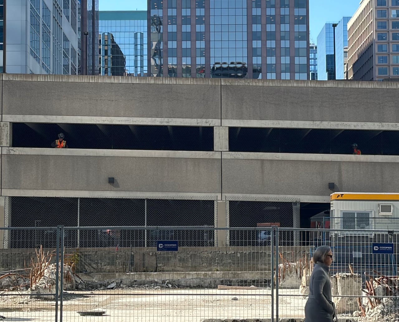 Two people in high-visibility vests and protective headgear inside a closed parking garage on an autumn day.