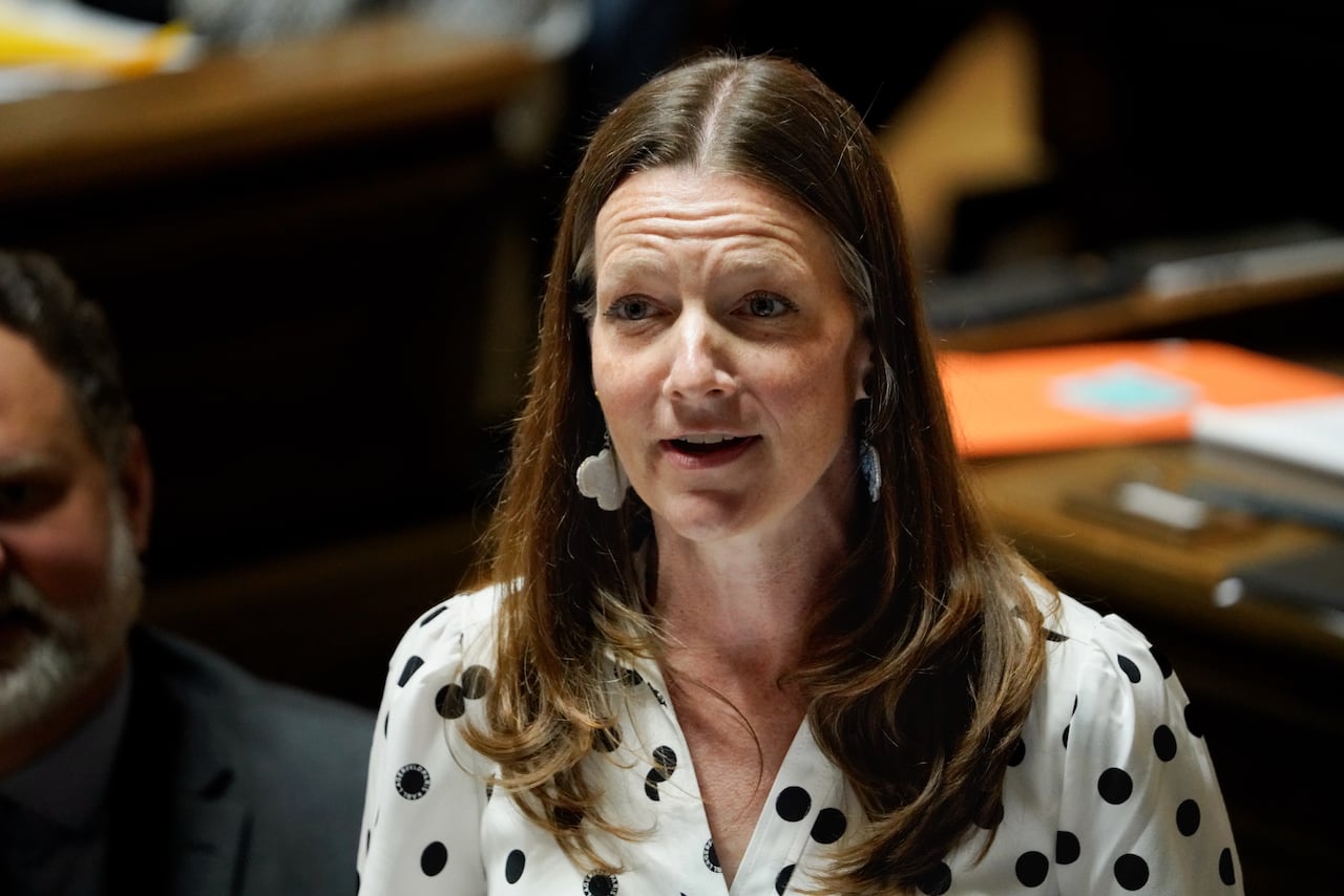 A woman in a black and white dress speaks during a government legislative session.
