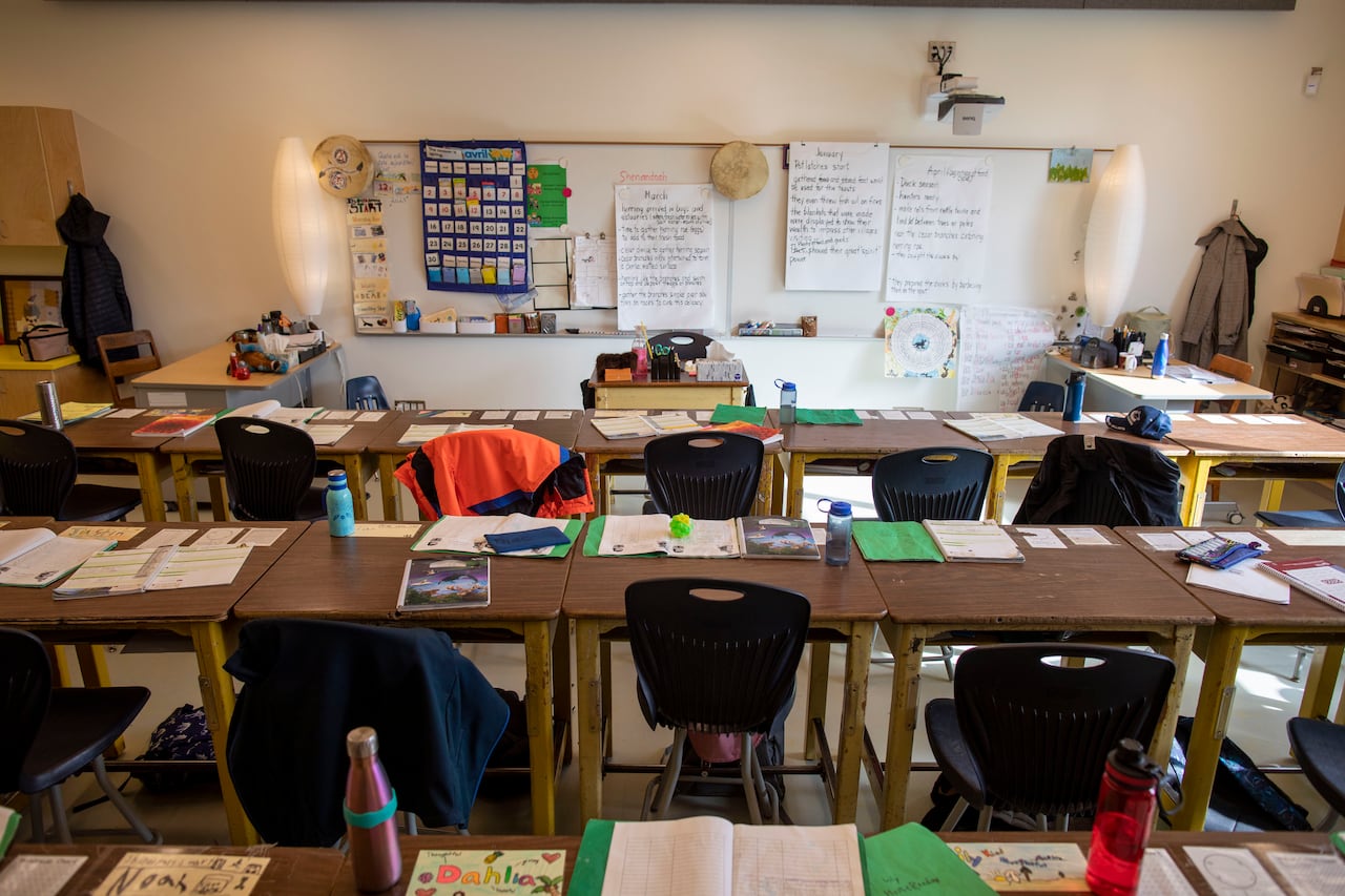A classroom with empty chairs and desks with notebooks on them.