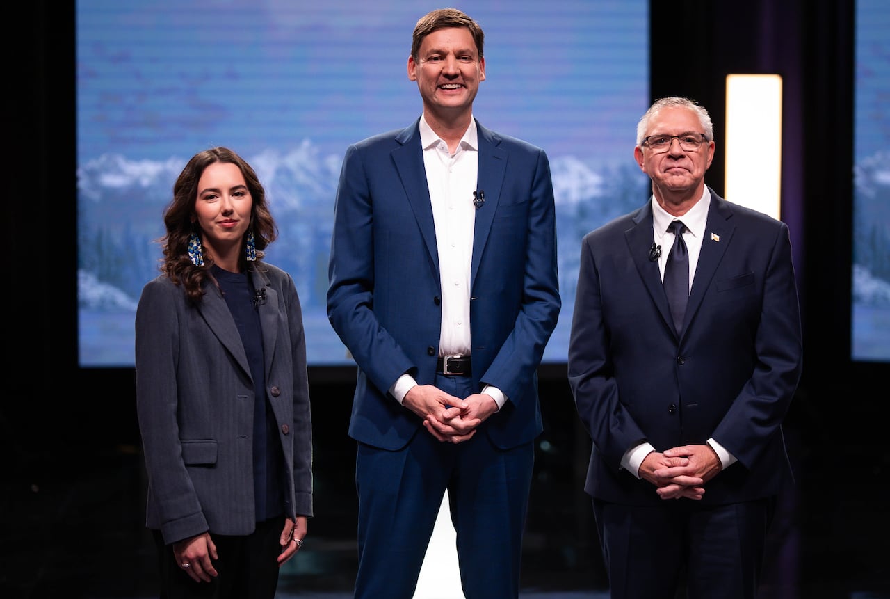A white woman and two white men smile in front of a mountain background.