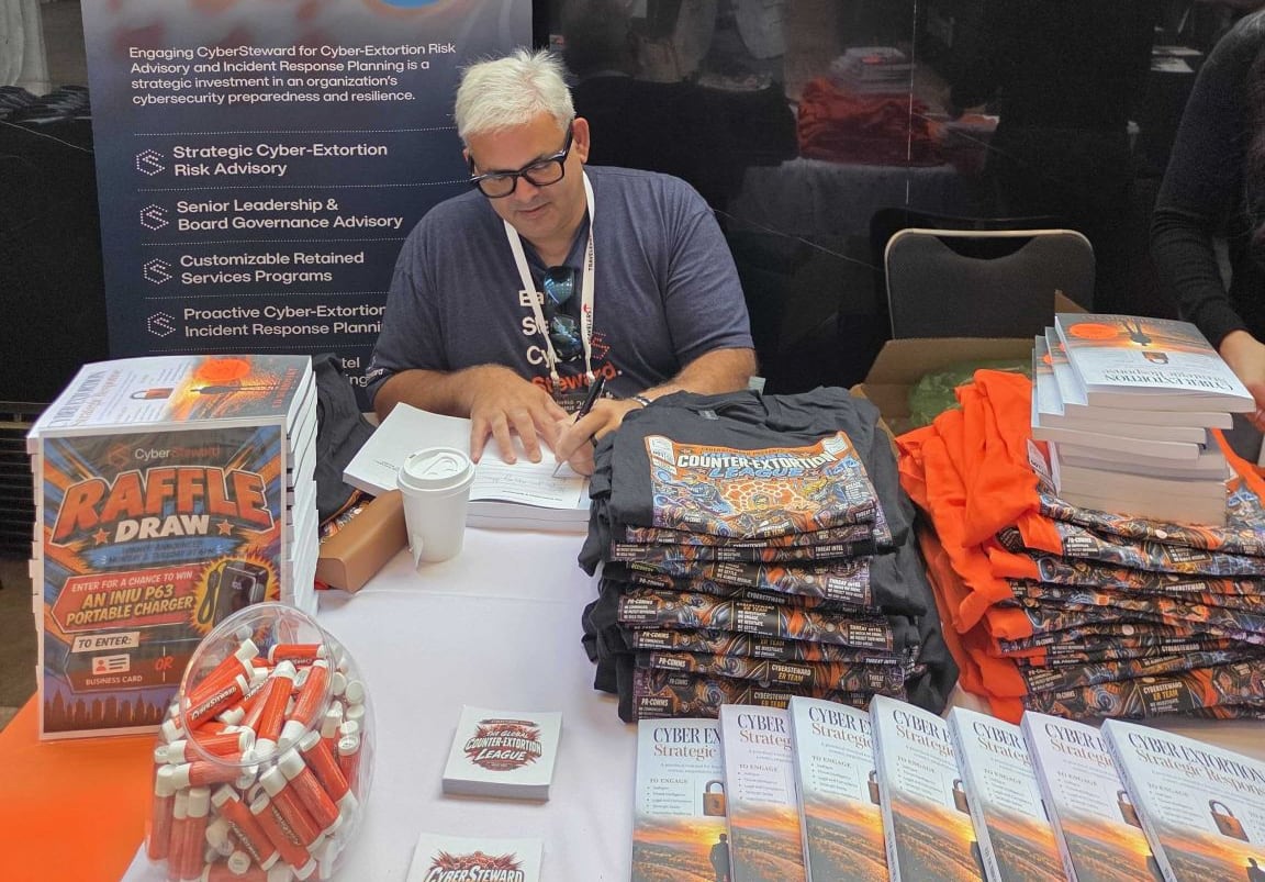 A man in a t-shirt, signing a stack of books