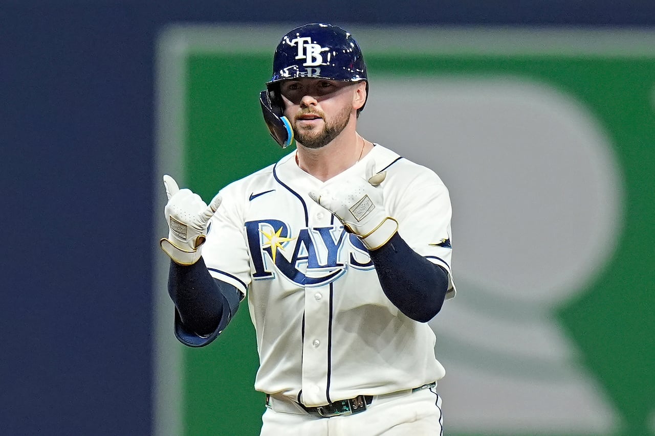 A man wearing a white baseball jersey and pants with the spelling "Rays" gestures with a rock and roll sign.