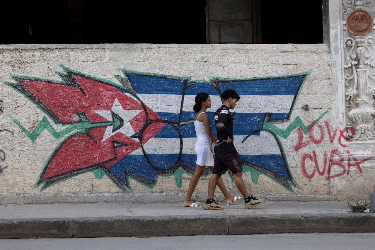 Two people walk past graffiti on a wall in Havana, Cuba.