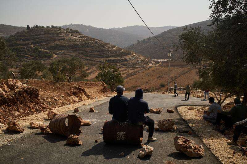 Palestinian men sit at a road, blocked in an effort to prevent Israeli settlers from entering the area, after settlers were spotted nearby in the West Bank town of Sinjil, Saturday, Oct. 24, 2026. (AP Photo/Leo Correa)