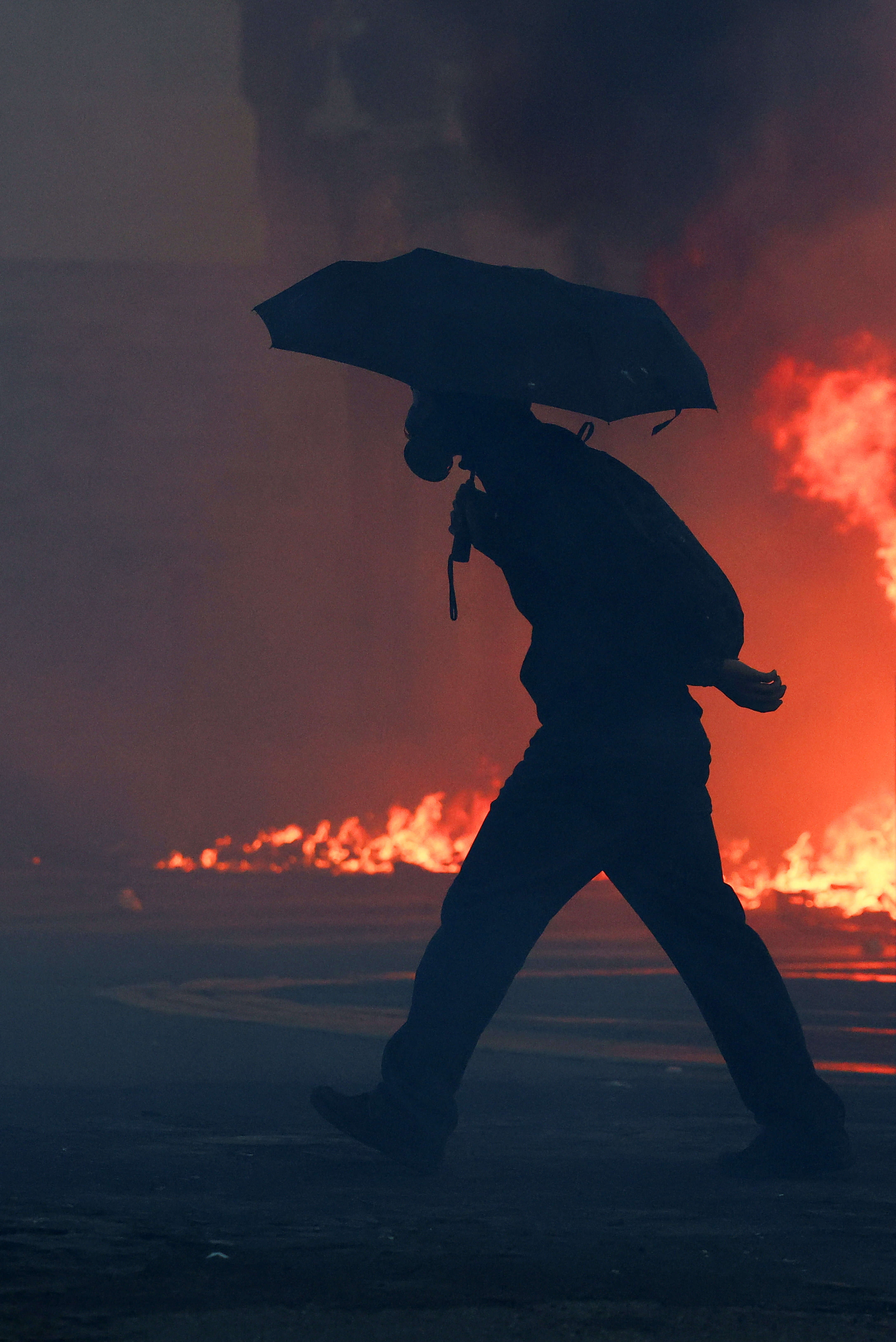 A protesters walks holding an umbrella next to a fire during an authorised demonstration organised by a labour union in Marseille. Second nationwide day of protests against the cost of living in France
