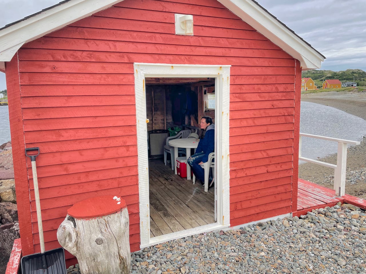 Lillian Saul is sitting inside a red fishing stage, looking away from the camera. There is a beach around the stage.