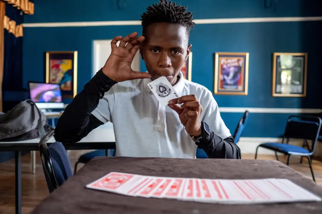 Duma Mgqoki, a student at the Cape Town College of Magic, practices a card trick in an empty classroom in 2021. In 2026, Mgqoki was killed in a gang-related shooting in the Philippi neighbourhood of Cape Town. Many of the College's students come from neighbourhoods rife with unemployment and violent crime.