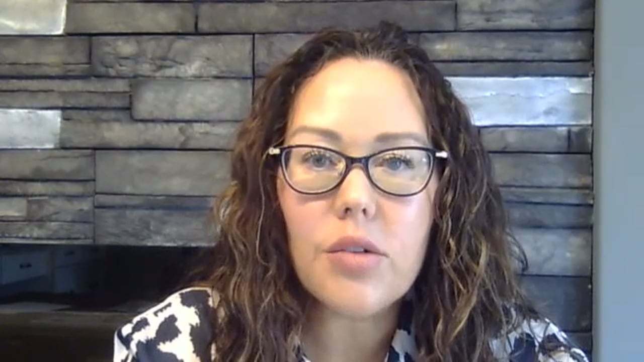 A woman with wavy hair is seen in a Zoom capture.