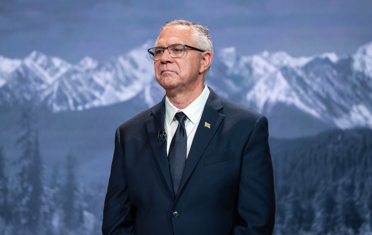 A white man is seen in front of a mountain background.