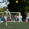 Standing on a green soccer field and wearing a yellow and light blue soccer uniform, Oleksandr “Sasha” Ostapchuk sets himself up to head a ball that's in the air while playing for a team of Ukrainian immigrants against a club with roots in Belarus at Tryzub Ukrainian American Sport Center in North Wales, Pennsylvania, on June 21.