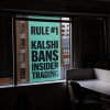 Viewed through the window of an office building, a giant banner for the prediction market platform Kalshi hangs on the outside of a building across the street on April 1. The banner says in all capital letters: "Rule #1 Kalshi bans insider trading."