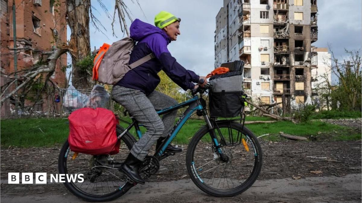 A woman cycles among destroyed buildings
