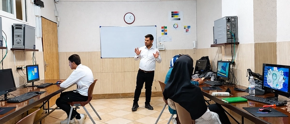 An instructor leads a computer training session in an Iranian classroom as students work at desktop computers.