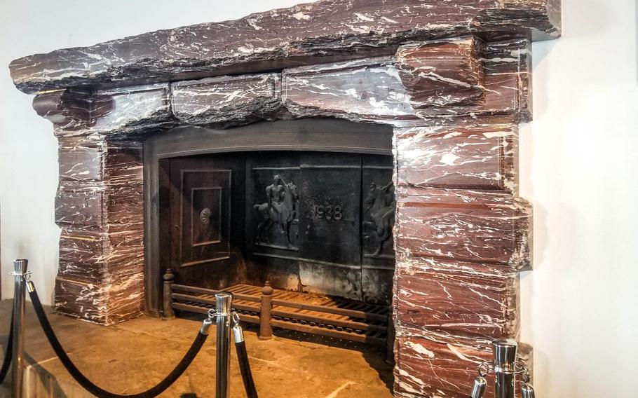 A large reddish-brown marble fireplace with white veins and a dark iron back stands behind black stanchions with a rope. 