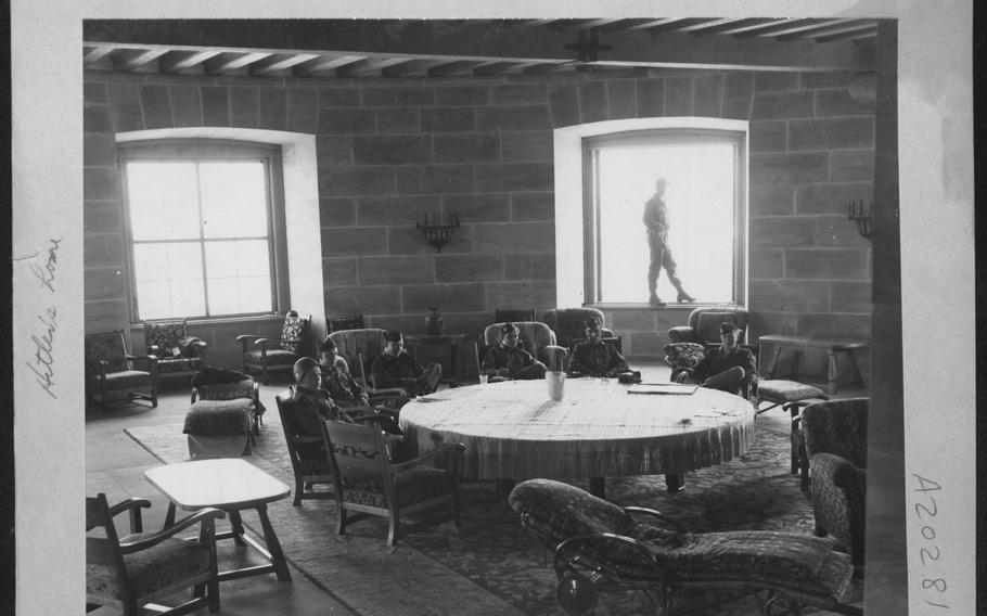 A black-and-white photo shows soldiers seated in armchairs around a round table in a stone room with large windows.
