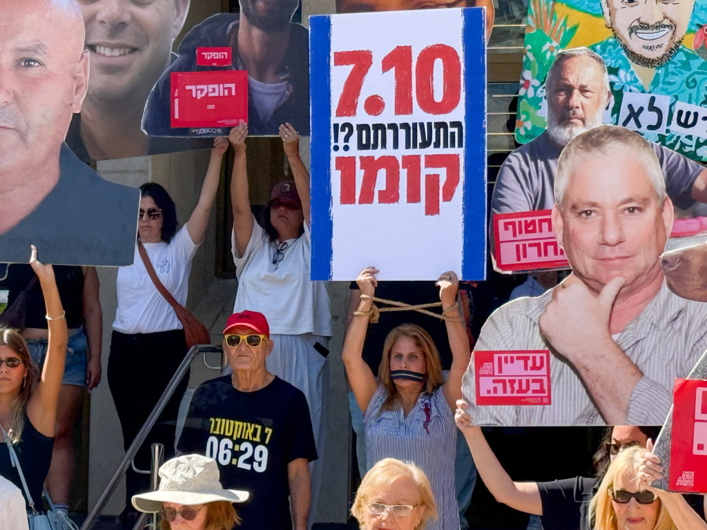 Protesters hold up pictures of slain Israeli hostages and a sign in Hebrew that says "7.10 did you wake up?! Rise up" on t...