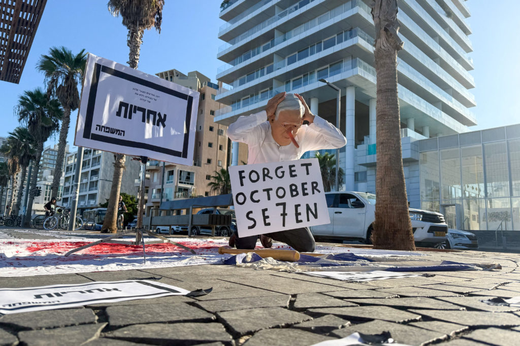 An anti-Netanyahu protester dressed as Israeli Prime Minister Benjamin Netanyahu kneels on a sheet covered with red paint,...