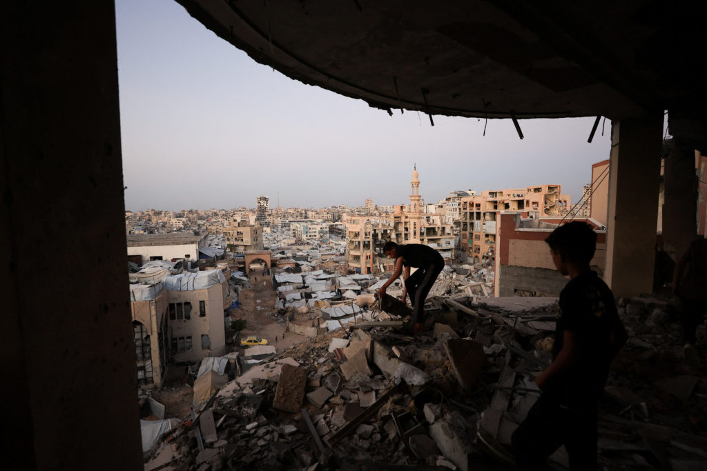 Palestinian man works amid the rubble of a building damaged during the war, overlooking a makeshift tent camp at the Islam...