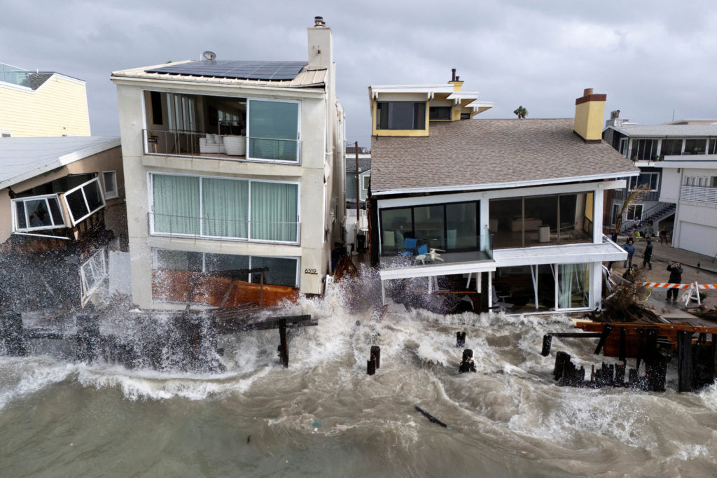 A drone view shows waves generated by Post-Tropical Cyclone Rachel as they impact houses along the coastline in Long Beach