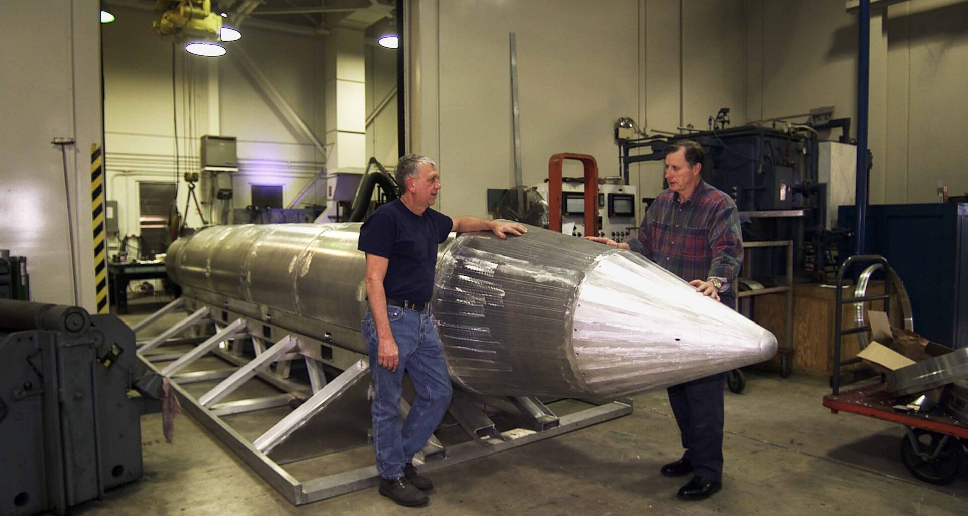 Al Weimorts, creator of the GU43/B Massive Ordnance Air Blast bomb, known colloquially as the Mother of All Bombs or MOAB, with Joseph Fellenz (left), lead model maker, looking over the prototype of the bomb before it was painted and tested, 2008. Image courtesy US DoD.