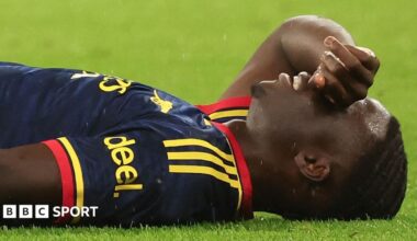 Bukayo Saka lying on grass with the back of his right hand held over his eyes