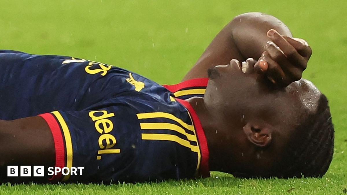 Bukayo Saka lying on grass with the back of his right hand held over his eyes