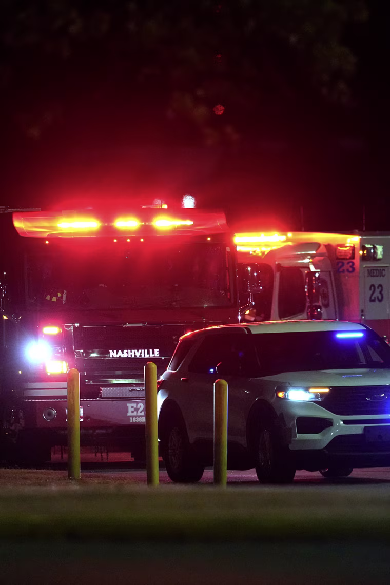 Red and blue emergency lights flashing atop ambulances as they pass through a parking turnstile.