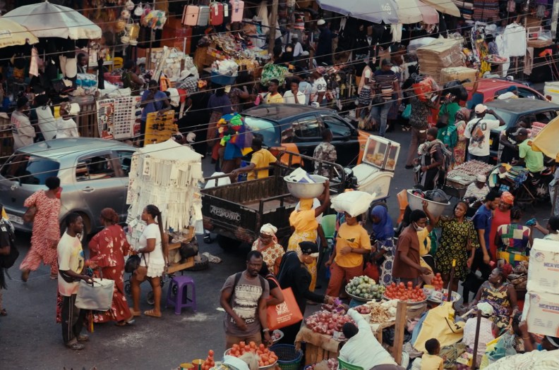 People and cars fill the street in a market.
