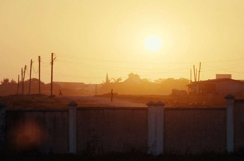 Two people are seen standing on the street at sunset.