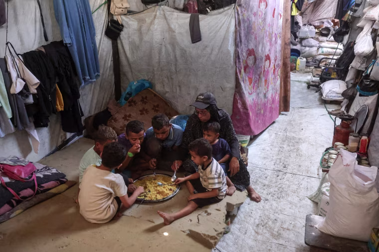 Image: A woman shares a plate of food provided by a charity kitchen with her children, in a camp in Khan Younis.
