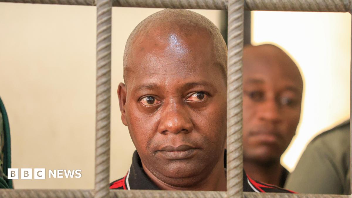 A close shot of a bald man looking through the bars of a cell