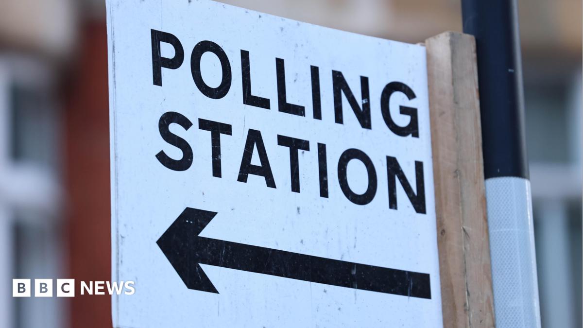 A polling station sign on a post. Polling station is written in black on a white background, with an arrow pointing to the left below the words