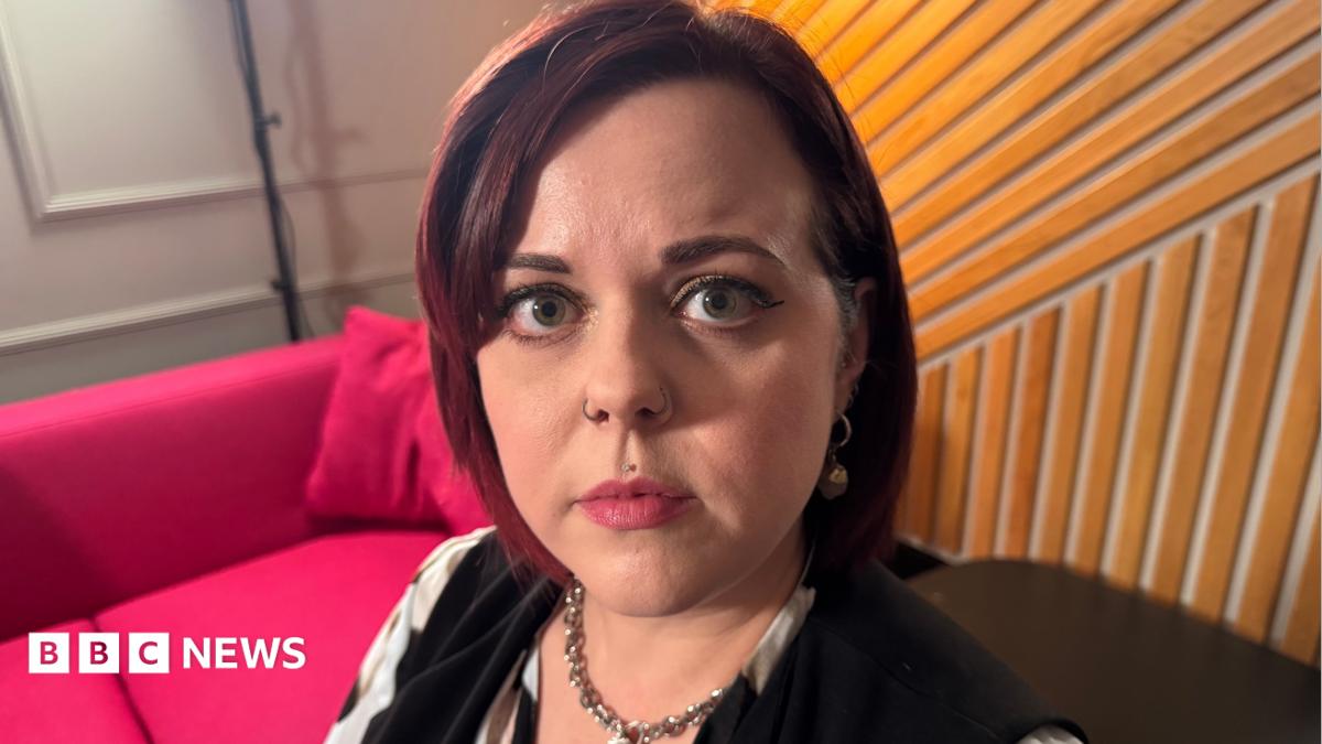 Headshot of Claire Milne, who has short dark hair, nose piercings and a piercing just above upper lip. She looks straight at the camera with a pensive expression on her face.