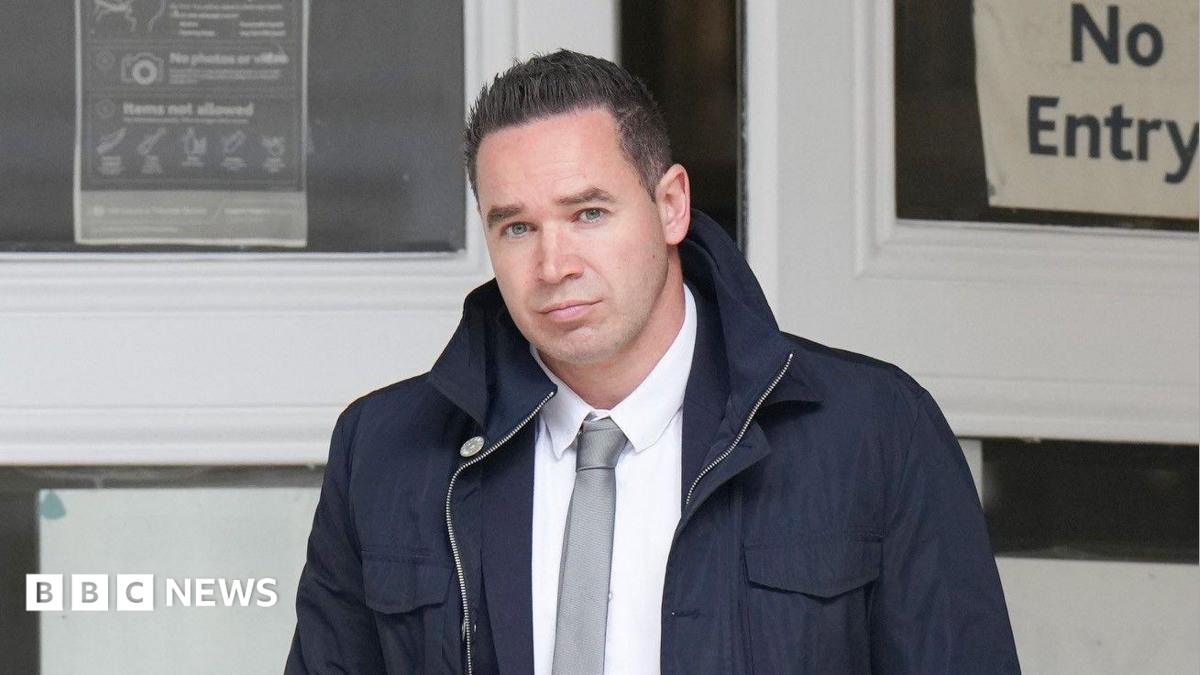A man with short black hair wearing a large dark blue coat. He is looking into and walking towards the camera.