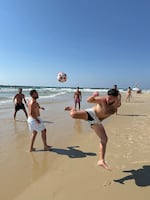 A group of friends kick a soccer ball back and forth in the air on the beach in Tel Aviv.