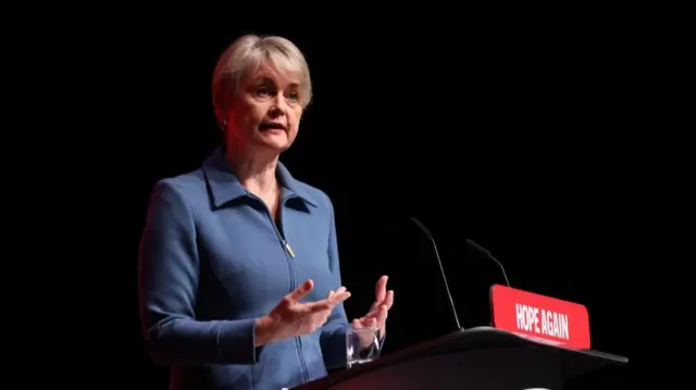 Yvette Cooper is pictured speaking at a podium, wearing a blue jacket.