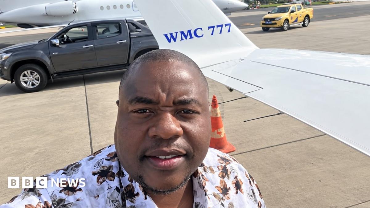 Wicknell Chivayo taking a selfie on an airport tarmac beside a small white aircraft marked “WMC 777.” A dark pick-up truck, a yellow airport vehicle and an orange traffic cone are visible behind him