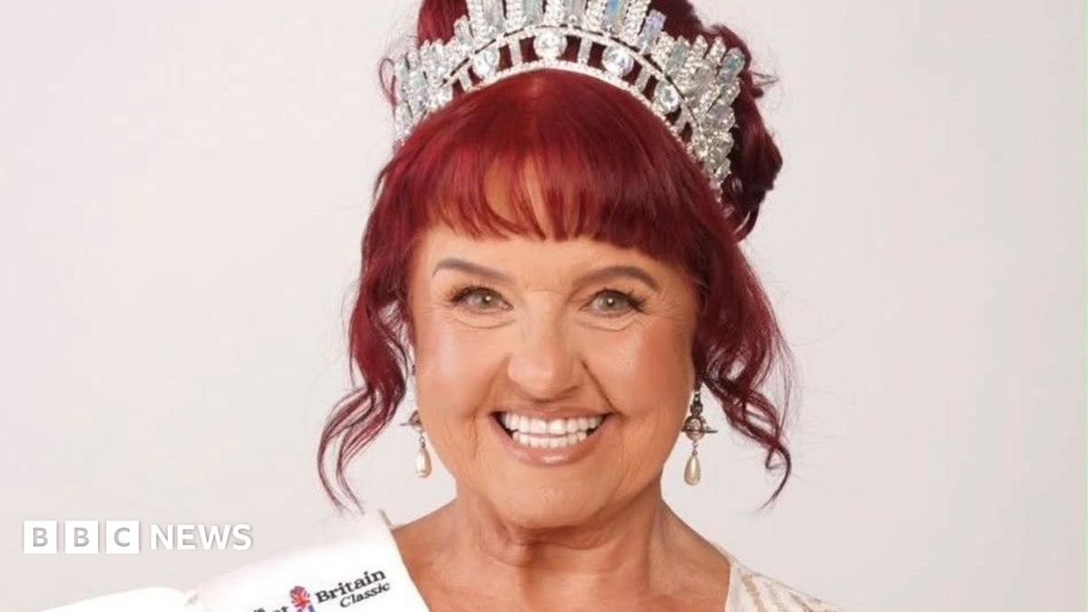 Ann Marie Harper wearing a tiara smiles at the camera. She has red hair in an updo and is wearing a white ballgown.