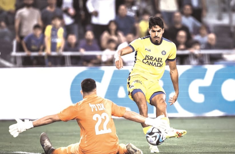 MACCABI TEL AVIV’s Dor Peretz shoots on Bnei Sakhnin ’keeper Mohammed Abu Nil in the yellow-and-blue’s 2-0 win in Israel Premier League action.