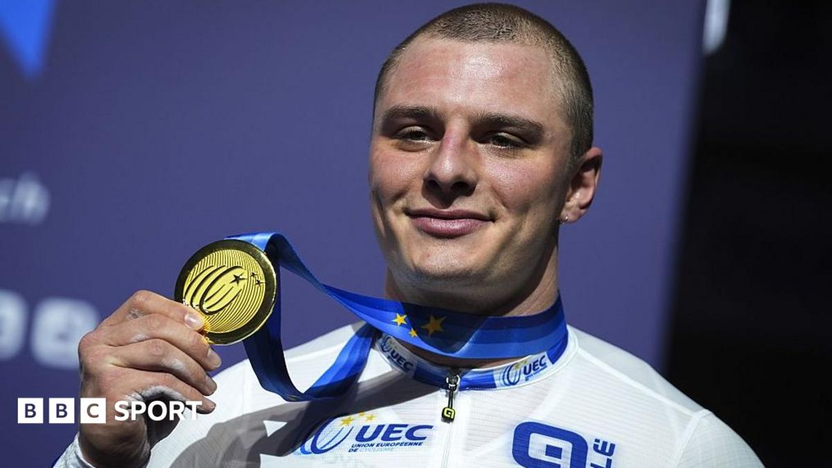GB cyclist Matt Richardson holds up a gold medal while smiling at the camera