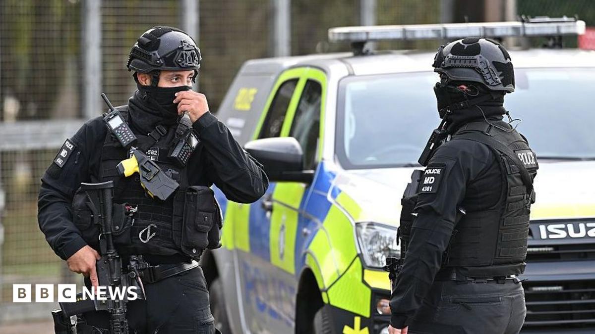 Two armed counter-terror police maintain road blocks and security checks around RAF Fairford both are wearing full black uniforms, helmets and are carrying guns.