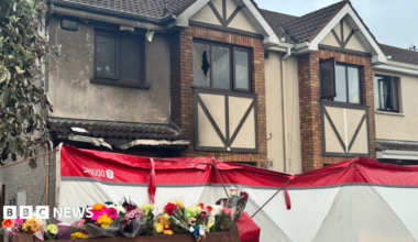 A house after a fire. Flowers and toys have been left outside.