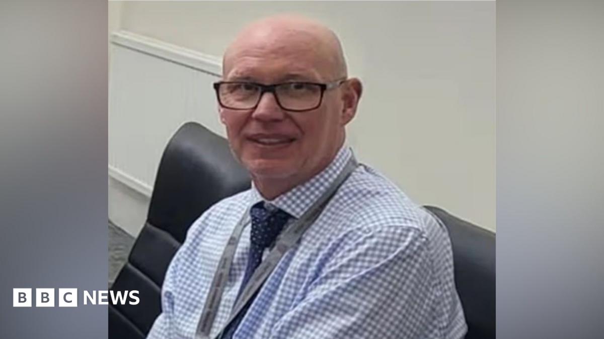 MI5 chief Sir Ken McCallum has short dark hair, dark glasses and is wearing a dark suit with a green tie.