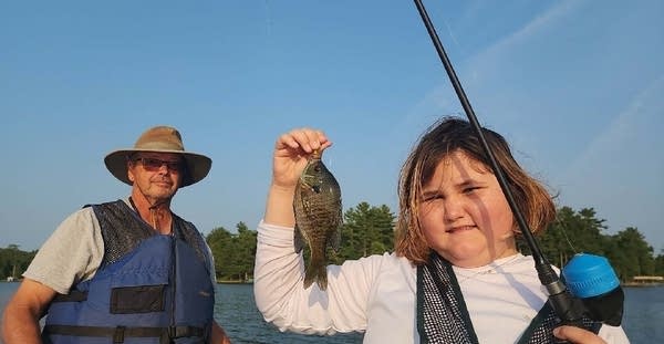 A man and a child are fishing, the child holds up a fish on a fishing line.