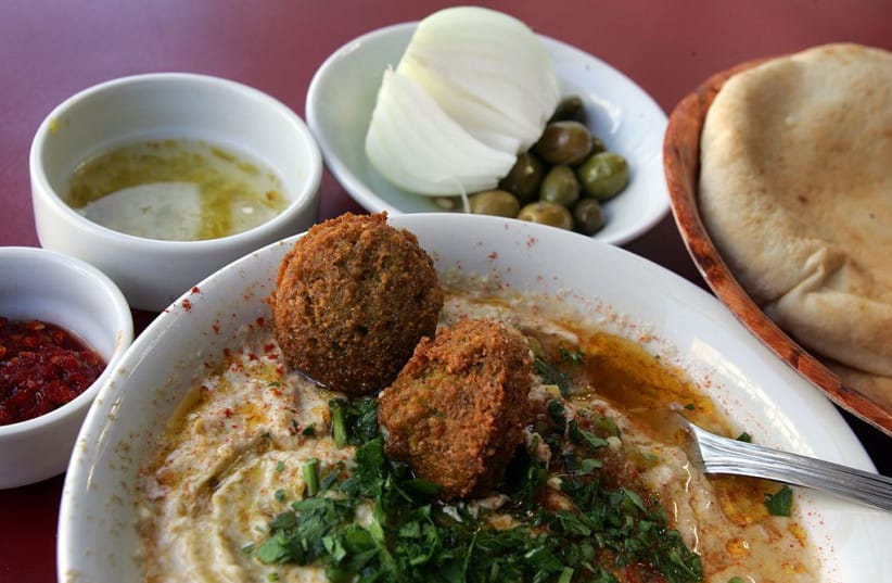 A bowl of hummous is served with olive oil, falafel balls and sprinkled with chopped parsley alongside fresh-baked pita bread, olives, a fresh onion, red chili paste and chili and lemon juice February 21, 2006 in a restaurant in Tel Aviv.