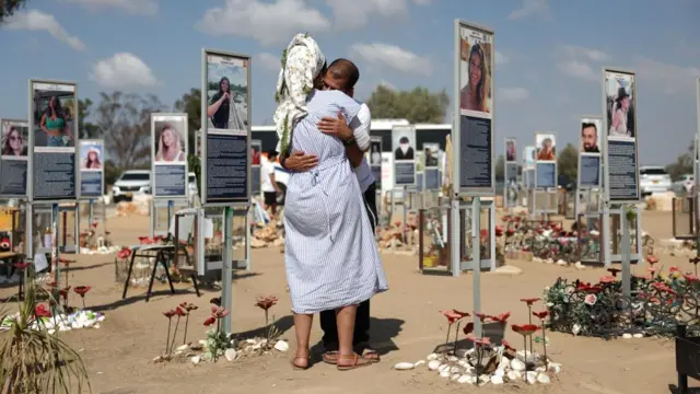 A man and woman hug in a memorial site which includes signposts of numerous victims of the 7 October Hamas attacks at the Nova music festival