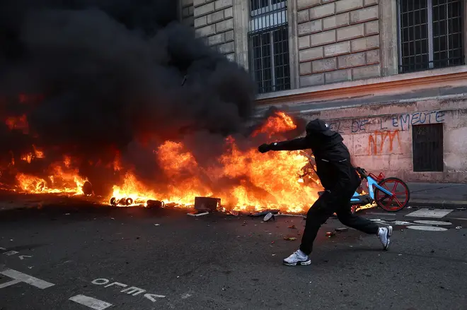 A masked protester throws an object onto a burning car in Paris