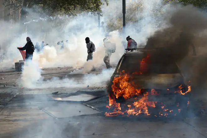 Protesters stand next to a burning car amid clashes during a demonstration at the Place de la Republique in Paris